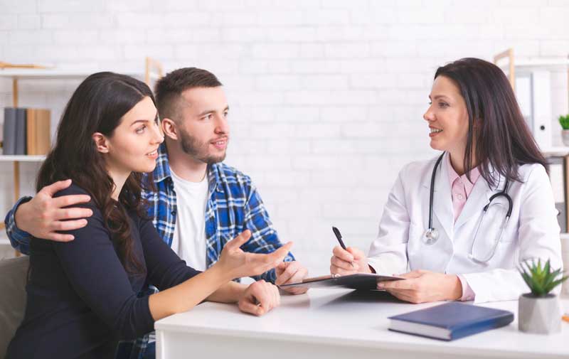 Woman and partner speaking with a female GP during a consultation